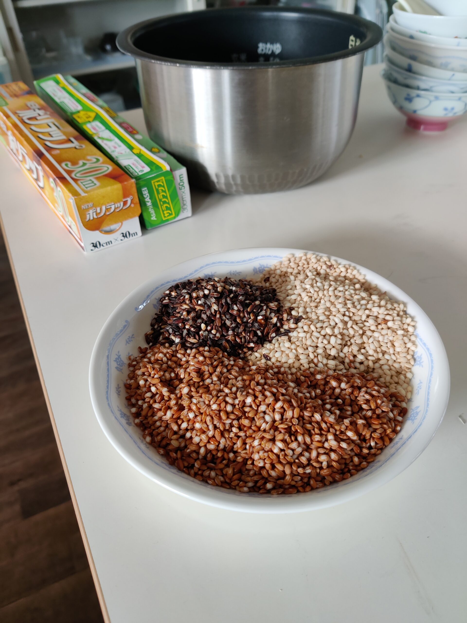 Bowel of three colours of ancient rice. Rice cooker bowel and clingfilm in the background.